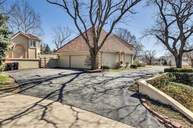 view of side of home with fence, aphalt driveway, a tiled roof, stucco siding, and an attached garage