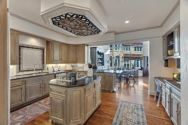 kitchen featuring a kitchen island, dark wood finished floors, stainless steel gas cooktop, a sink, and dark countertops