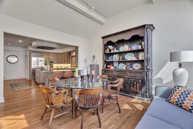 dining space with lofted ceiling with beams, baseboards, track lighting, and light wood finished floors