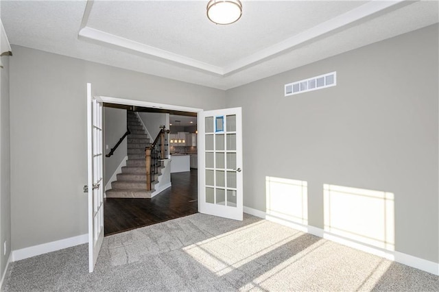 spare room featuring carpet floors, a raised ceiling, visible vents, and stairway