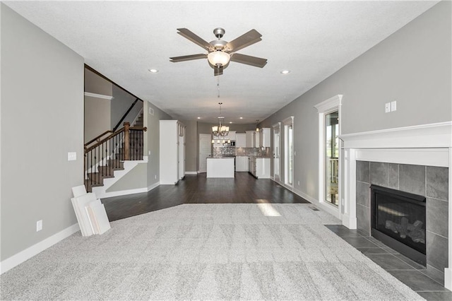 unfurnished living room with recessed lighting, ceiling fan with notable chandelier, a fireplace, baseboards, and stairway