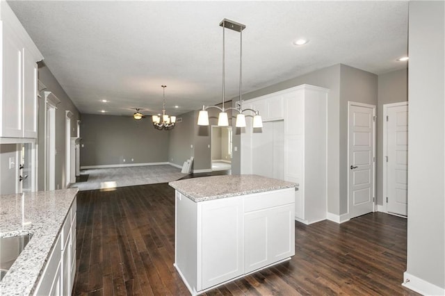 kitchen featuring light stone countertops, dark wood-style floors, white cabinets, and decorative light fixtures