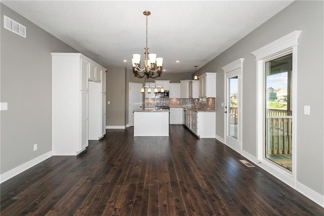 interior space with a center island, dark wood-style flooring, a notable chandelier, visible vents, and decorative backsplash