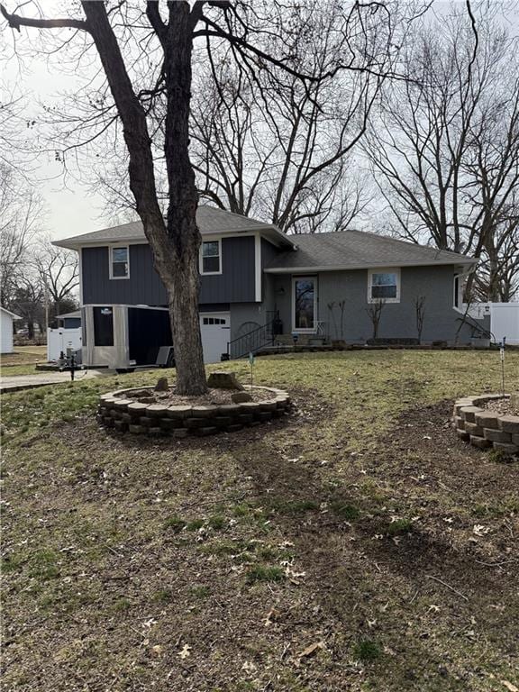 back of property featuring a lawn, an attached garage, an outdoor fire pit, and fence