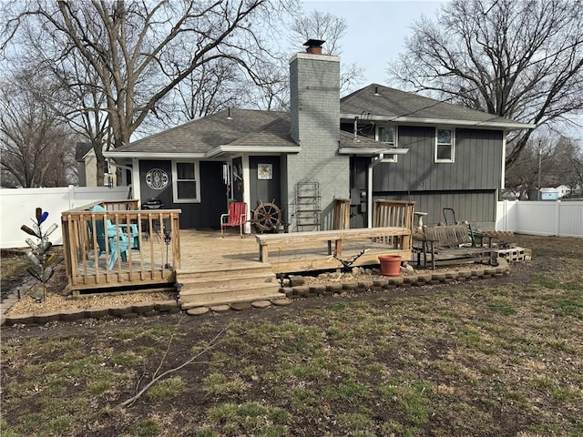 rear view of property with a shingled roof, a chimney, a deck, and fence