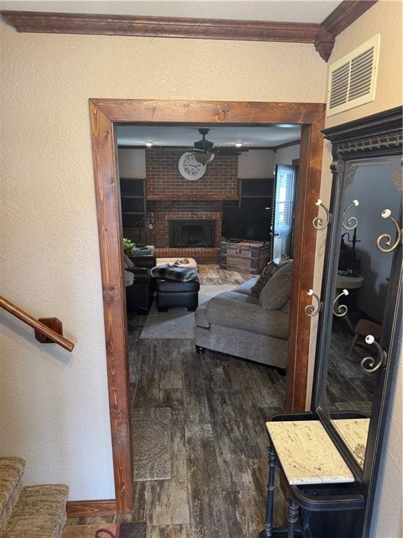 living area with visible vents, wood finished floors, crown molding, a brick fireplace, and stairs