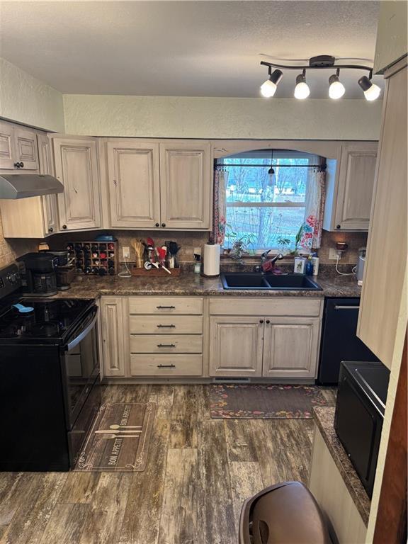 kitchen with dark wood-style floors, a sink, black appliances, under cabinet range hood, and dark countertops