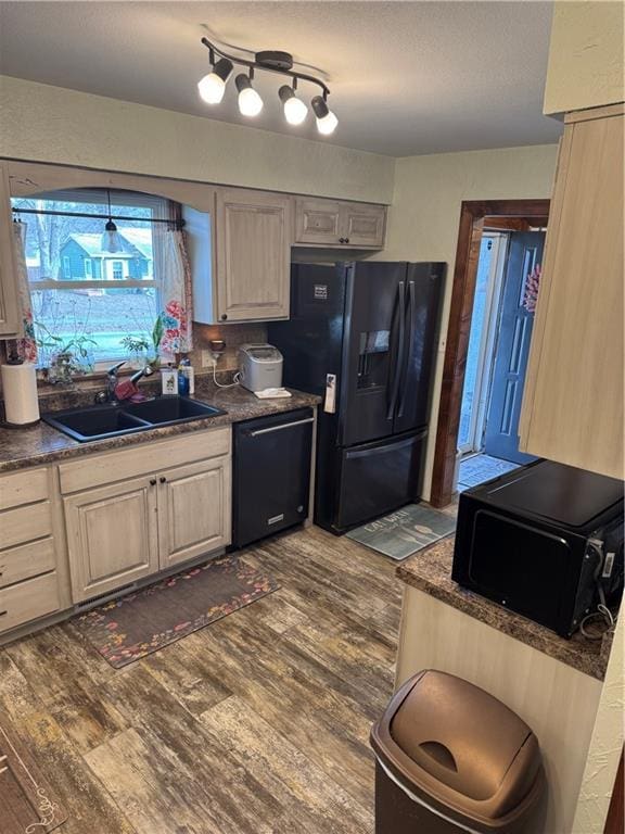 kitchen with a sink, dark countertops, black appliances, and dark wood finished floors