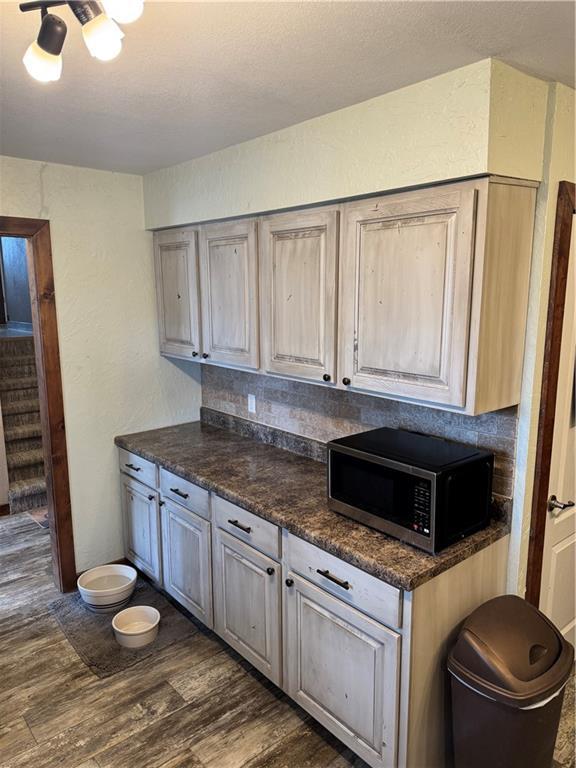 kitchen with stainless steel microwave, dark countertops, dark wood-style floors, and a textured wall