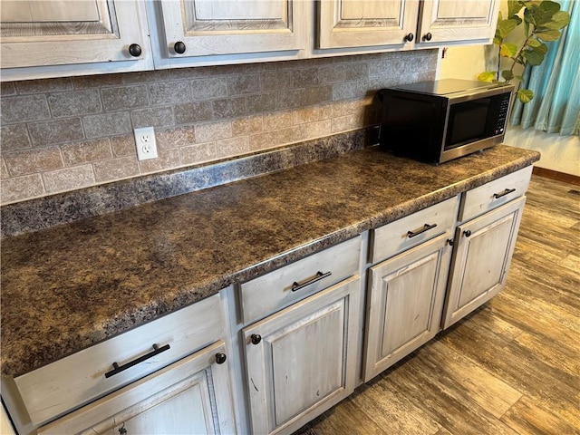 kitchen with stainless steel microwave, dark countertops, dark wood-style floors, and backsplash