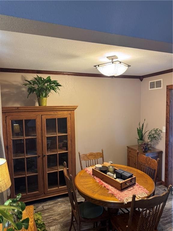 dining area with a textured ceiling, wood finished floors, visible vents, and ornamental molding