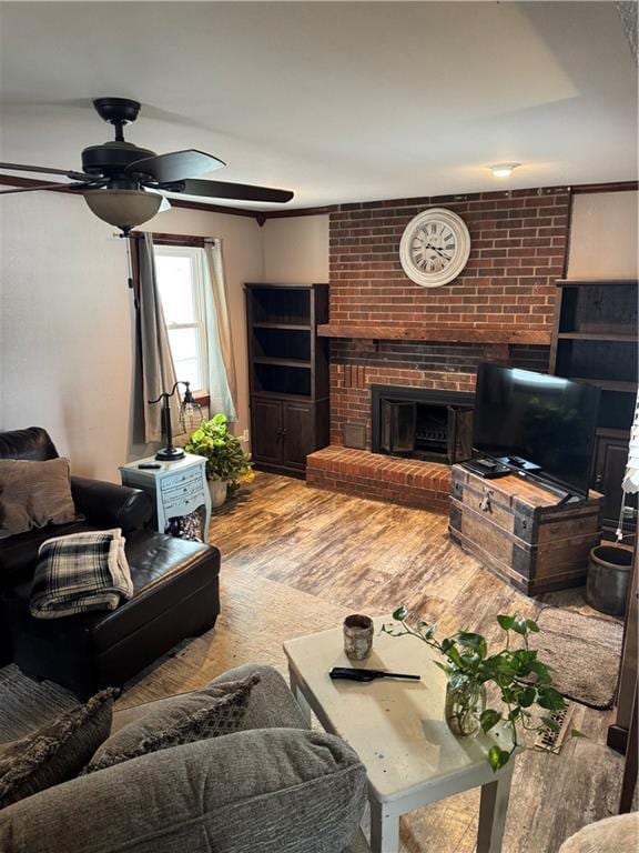 living room featuring a brick fireplace, wood finished floors, and a ceiling fan