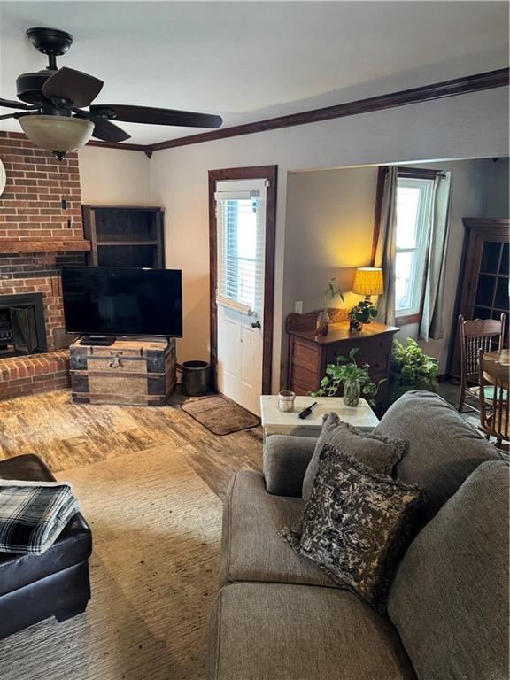 living area featuring plenty of natural light, a fireplace, crown molding, and ceiling fan