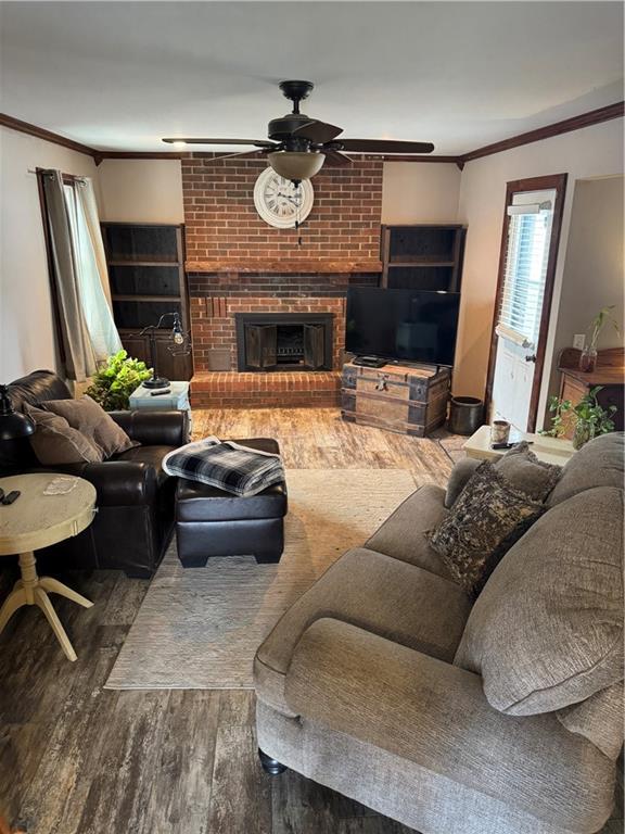 living area featuring a fireplace, crown molding, a ceiling fan, and wood finished floors