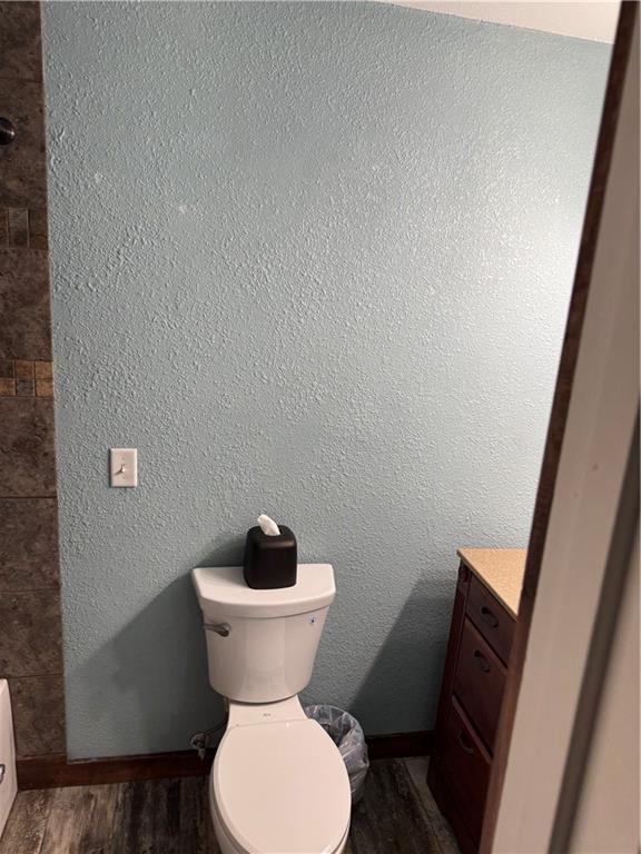 bathroom featuring baseboards, toilet, a textured wall, wood finished floors, and vanity