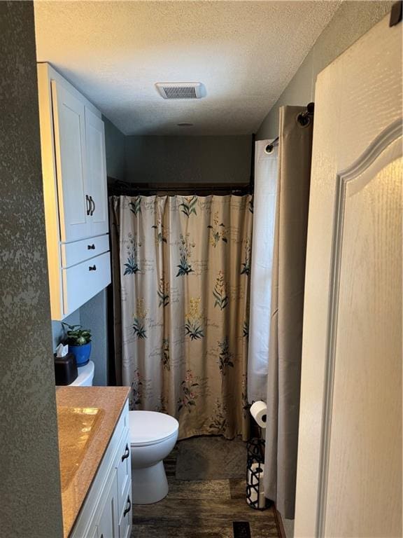 full bathroom with visible vents, toilet, a textured ceiling, wood finished floors, and vanity