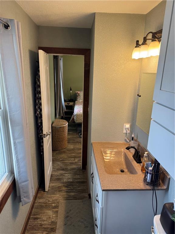 ensuite bathroom featuring ensuite bath, vanity, a textured wall, and wood finished floors