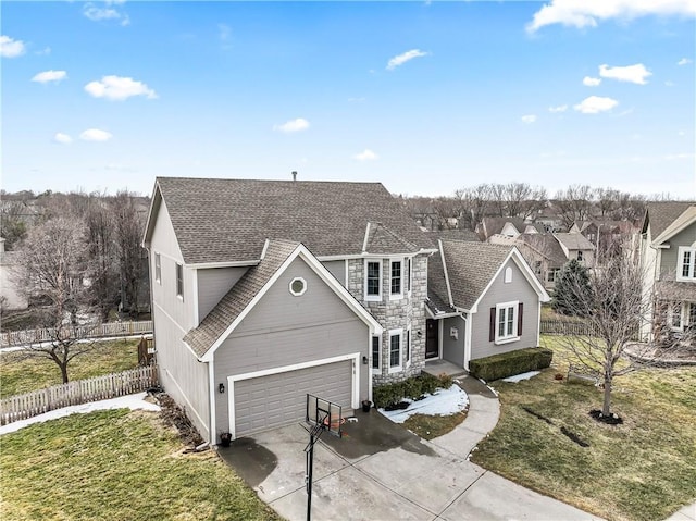 traditional-style house featuring a shingled roof, concrete driveway, stone siding, fence, and a front lawn