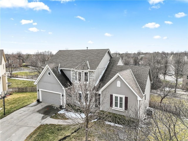 traditional-style home with a garage, a shingled roof, concrete driveway, fence, and a front yard