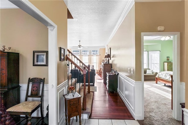 entrance foyer featuring a textured ceiling, a decorative wall, a wainscoted wall, stairway, and crown molding