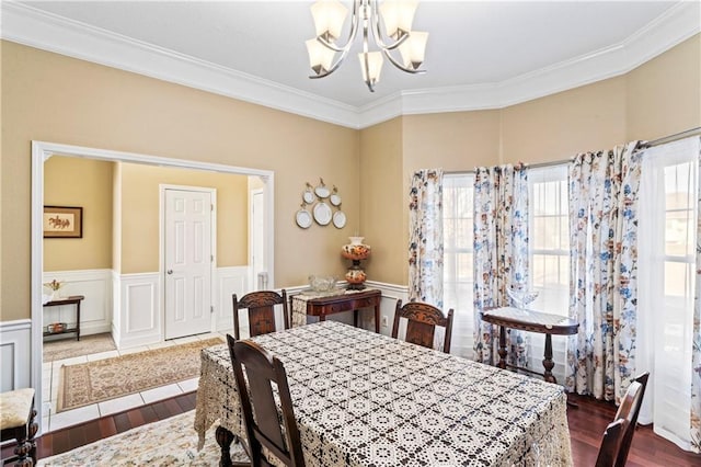 dining space with dark wood-style floors, ornamental molding, a wainscoted wall, and a notable chandelier