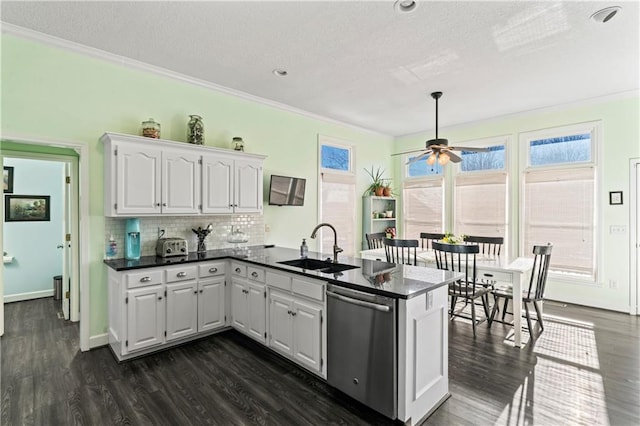 kitchen with dark countertops, a sink, a peninsula, and stainless steel dishwasher