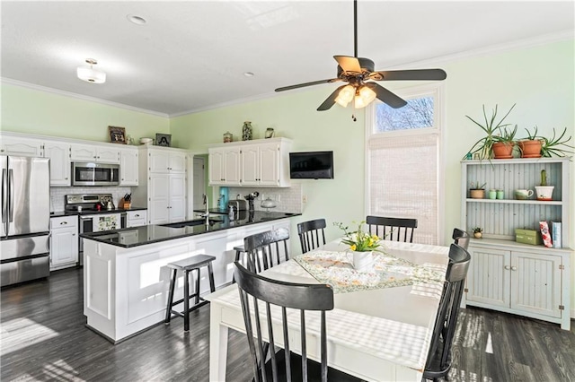 kitchen with dark countertops, ornamental molding, stainless steel appliances, white cabinetry, and a sink