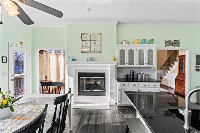 bar featuring decorative backsplash, a glass covered fireplace, dark wood-style floors, stairs, and crown molding