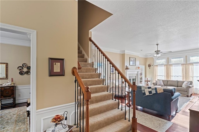 living room with a fireplace, crown molding, stairway, a ceiling fan, and a textured ceiling