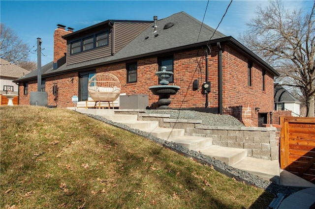 rear view of property featuring brick siding, a chimney, a yard, and a shingled roof