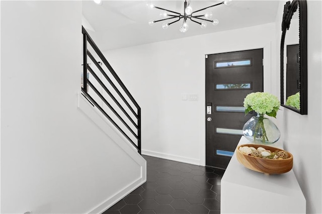 foyer entrance featuring stairs, dark tile patterned flooring, baseboards, and a chandelier