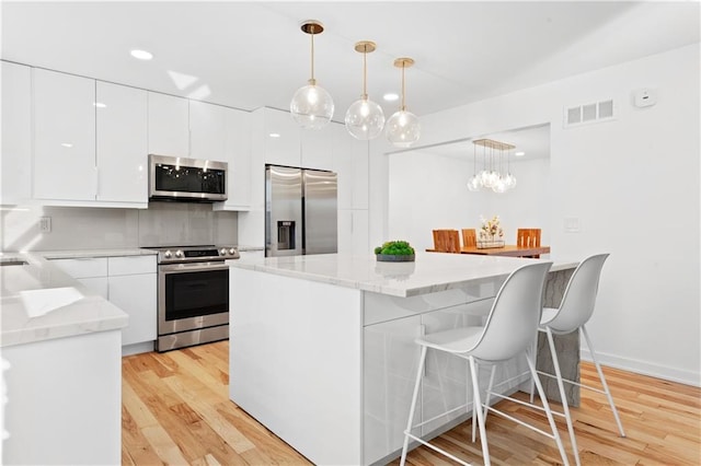 kitchen with light wood finished floors, stainless steel appliances, hanging light fixtures, white cabinets, and tasteful backsplash