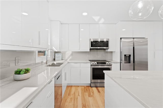 kitchen with a sink, light stone counters, appliances with stainless steel finishes, white cabinetry, and modern cabinets