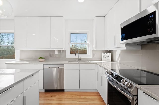 kitchen with a sink, stainless steel appliances, light wood-style floors, and white cabinetry