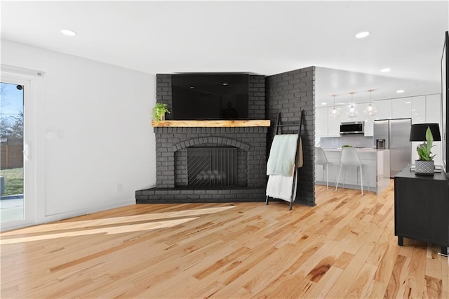 unfurnished living room featuring a brick fireplace, recessed lighting, and light wood finished floors