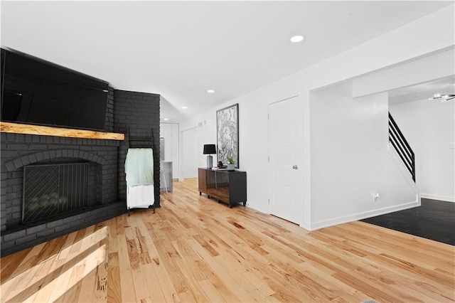 unfurnished living room featuring wood finished floors, recessed lighting, a fireplace, baseboards, and stairs