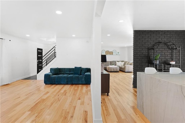 living area with recessed lighting, a brick fireplace, wood finished floors, and stairs