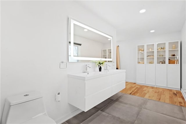 full bath with toilet, a sink, wood finished floors, recessed lighting, and double vanity