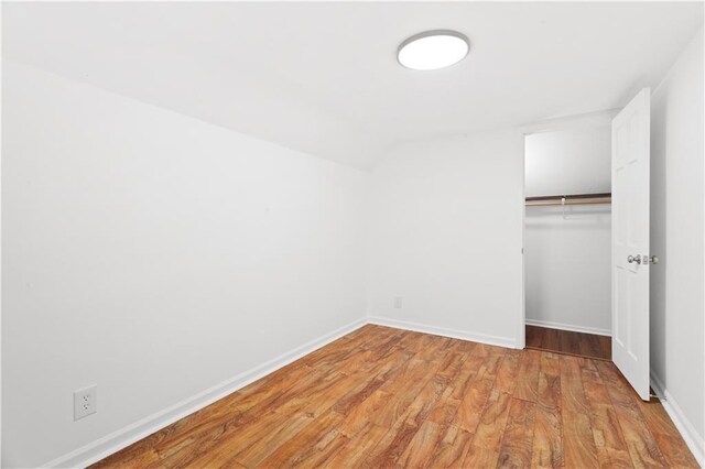 unfurnished bedroom featuring a closet, light wood-style flooring, baseboards, and vaulted ceiling