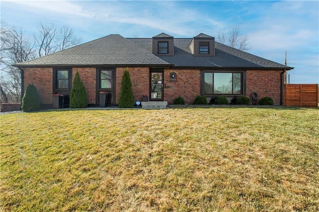 view of front facade featuring brick siding, a shingled roof, a front yard, and fence