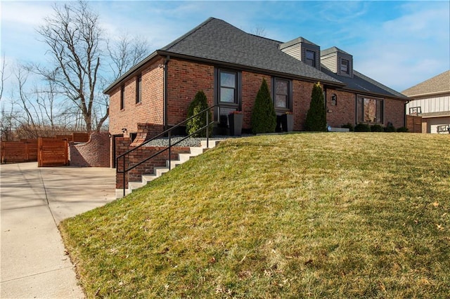 view of front of property featuring driveway, a front lawn, fence, roof with shingles, and brick siding