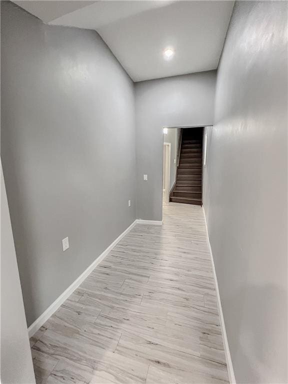 corridor with light wood finished floors, stairs, and baseboards