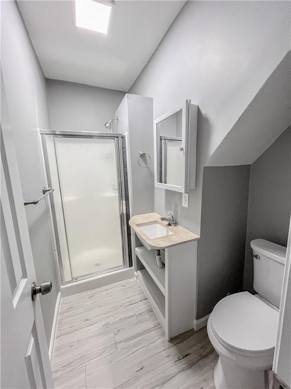 full bath with toilet, wood finished floors, vanity, baseboards, and a stall shower