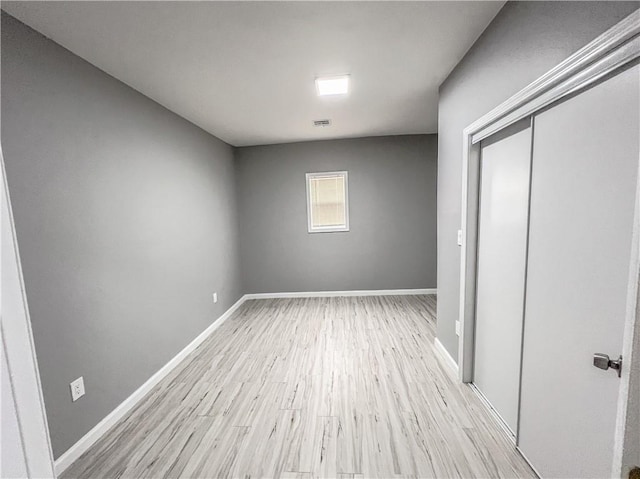 unfurnished bedroom featuring visible vents, a closet, light wood-style flooring, and baseboards