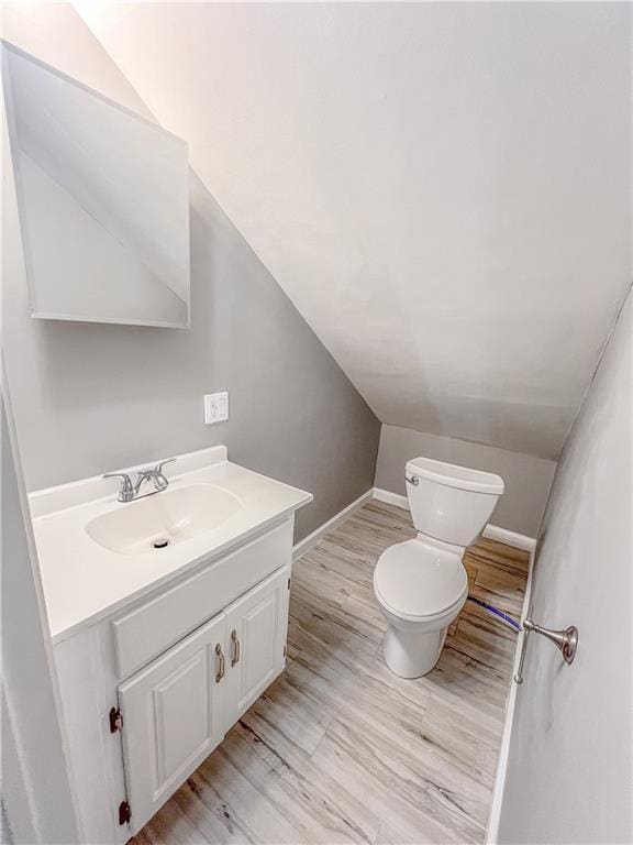 bathroom featuring toilet, wood finished floors, vanity, baseboards, and vaulted ceiling