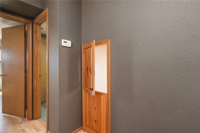 hall featuring light wood-type flooring and a textured wall