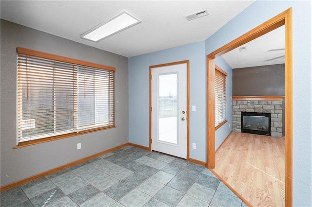 foyer with a stone fireplace, visible vents, and baseboards