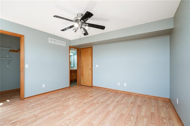 unfurnished bedroom with a spacious closet, visible vents, baseboards, wood finished floors, and a closet