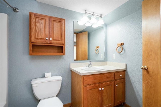 bathroom featuring toilet, vanity, and a textured wall