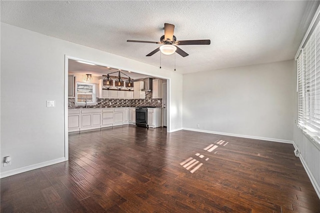 unfurnished living room with baseboards, ceiling fan with notable chandelier, dark wood-style flooring, and a sink